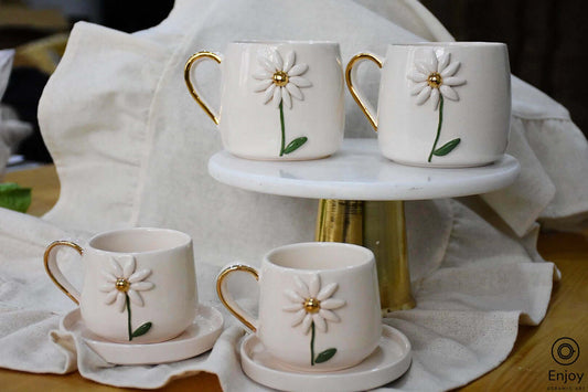 Four ceramic mugs with daisy designs and gold accents, elegantly displayed on a marble stand.