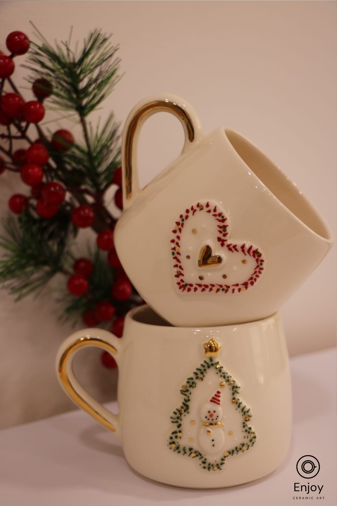 Two ceramic mugs with decorative designs on a white surface with a Christmas-themed background.