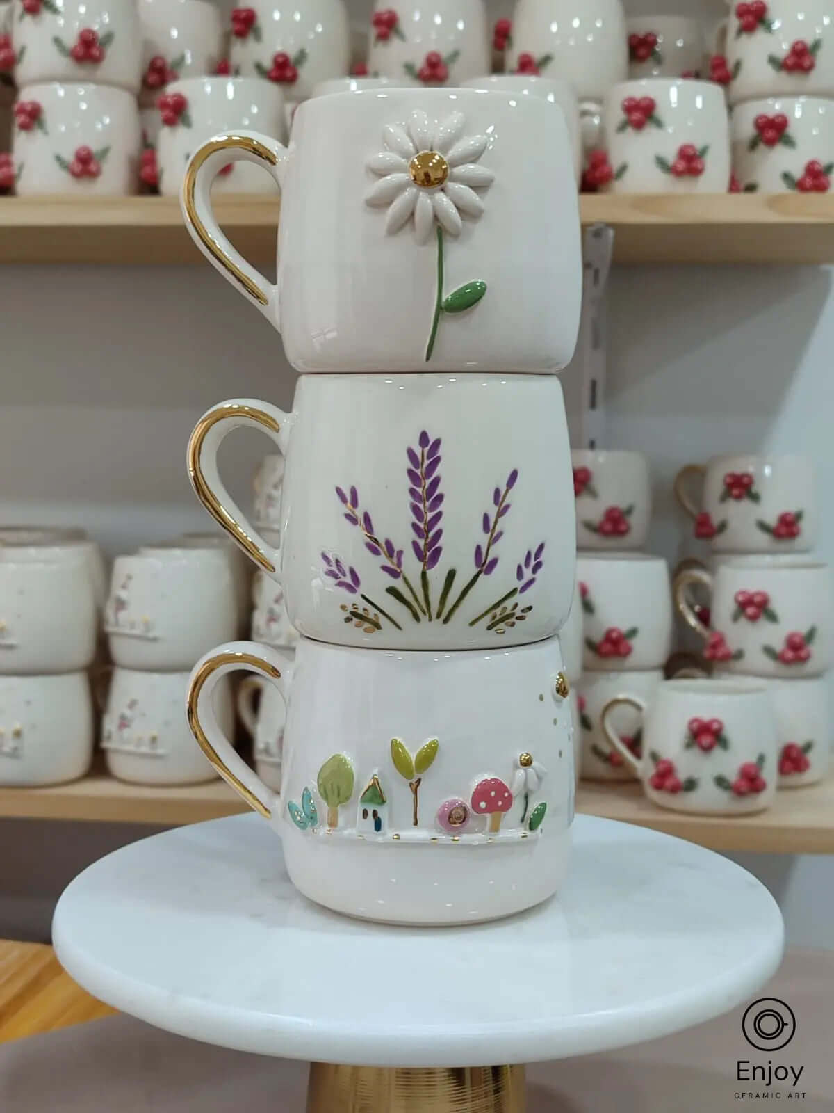 Set of three handmade ceramic mugs featuring daisy, lavender, and fairy garden designs, each with gold handles and detailing.