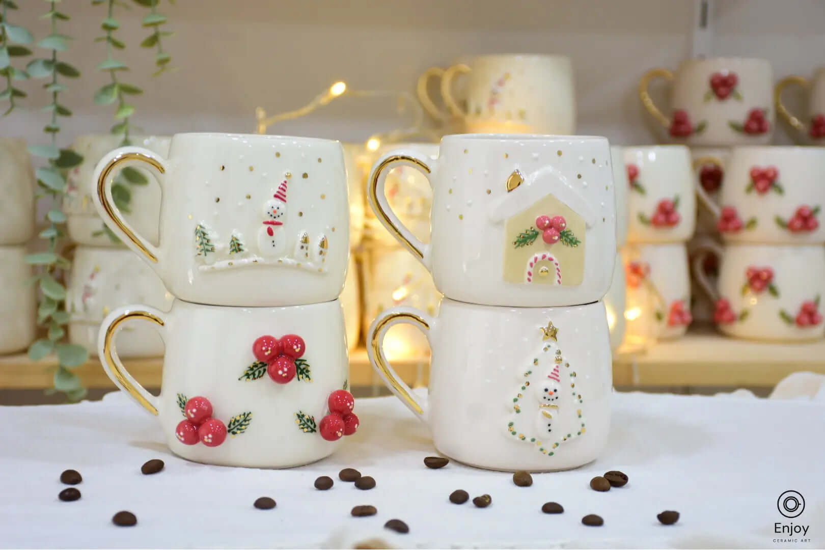 A festive set of four ceramic mugs, each with holiday-themed designs, featuring snowmen, holly berries, a gingerbread house, and a decorated tree.