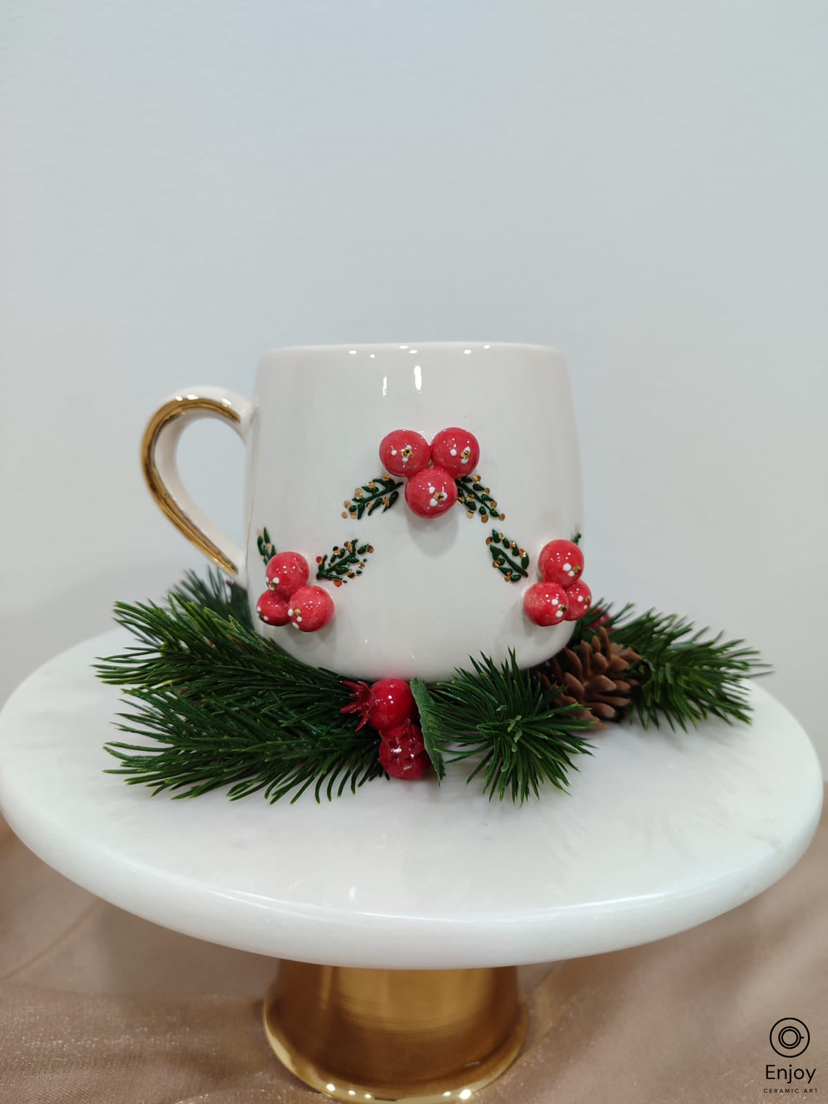 Handmade white mug with 3d red winterberies mug with gold handle on a pine branch with a white background