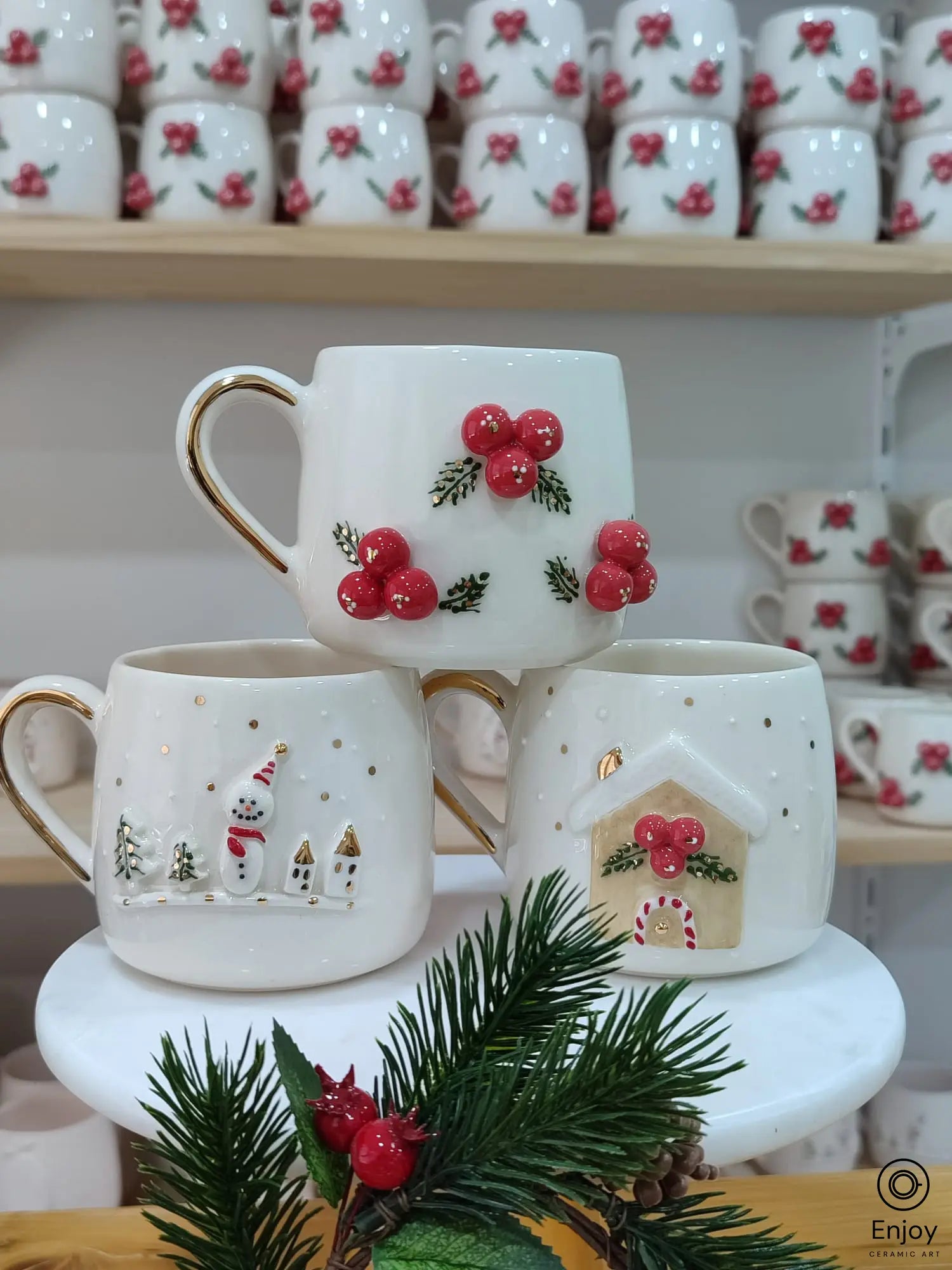 Handmade ceramic Christmas mug set featuring a snowman, winterberries, and a gingerbread house design with gold accents and handles.