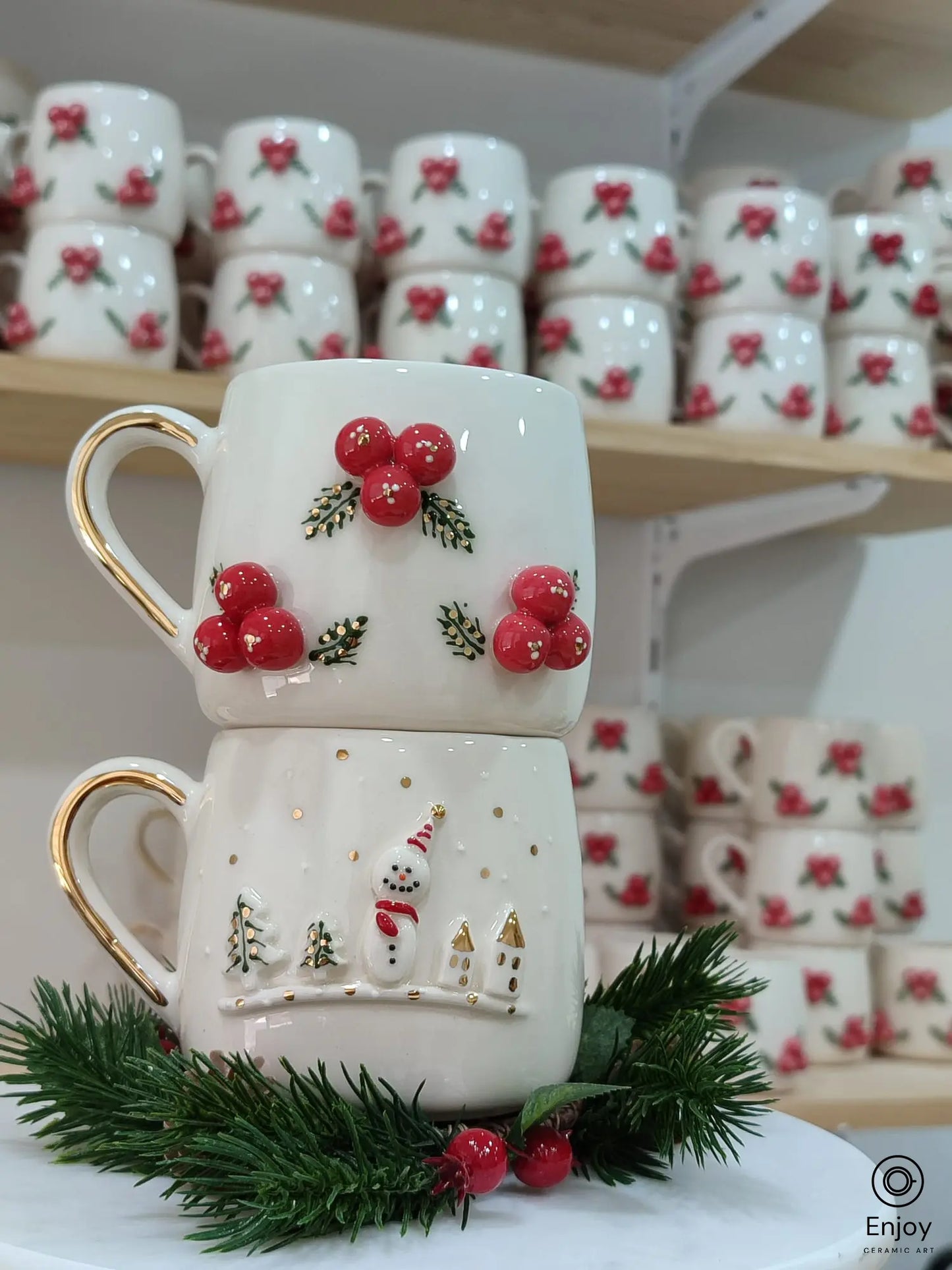 Handmade ceramic Christmas mug set featuring a snowman with a red scarf and a 3D winterberry design, both with gold accents and handles, perfect for holiday gifting.