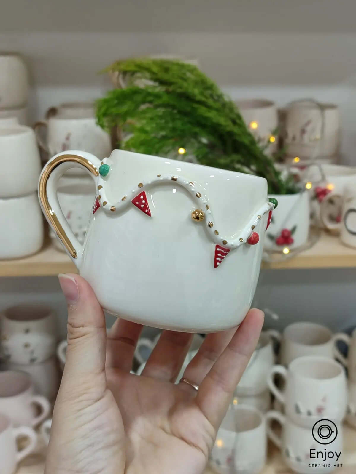 A handmade ceramic mug featuring a festive garland design with red, green, and gold accents and a gold handle, perfect for holiday celebrations and gifts.