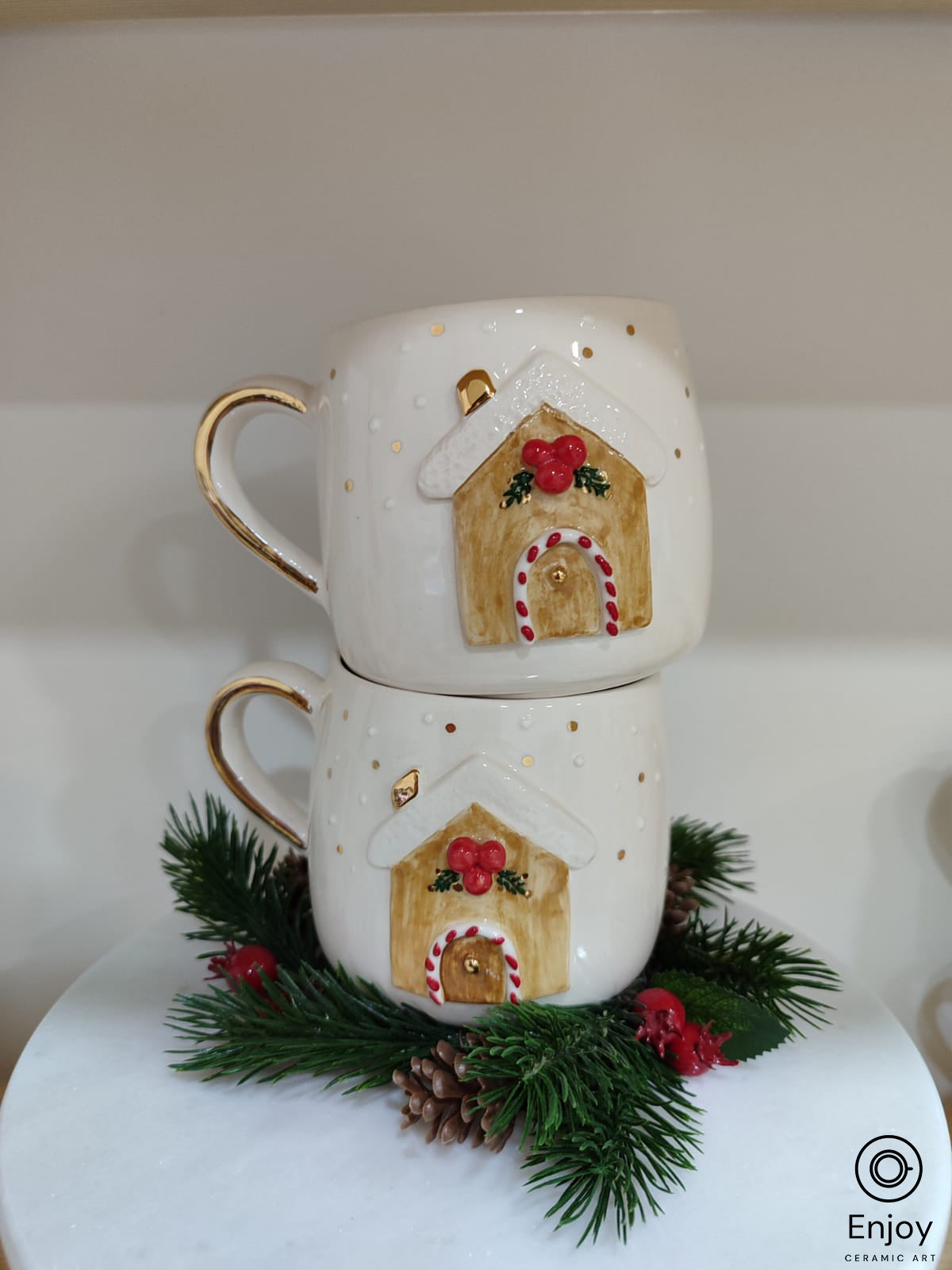 2 stacked up chic white mugs adorned with 3D gingerbread house design, resting on a green pine branch