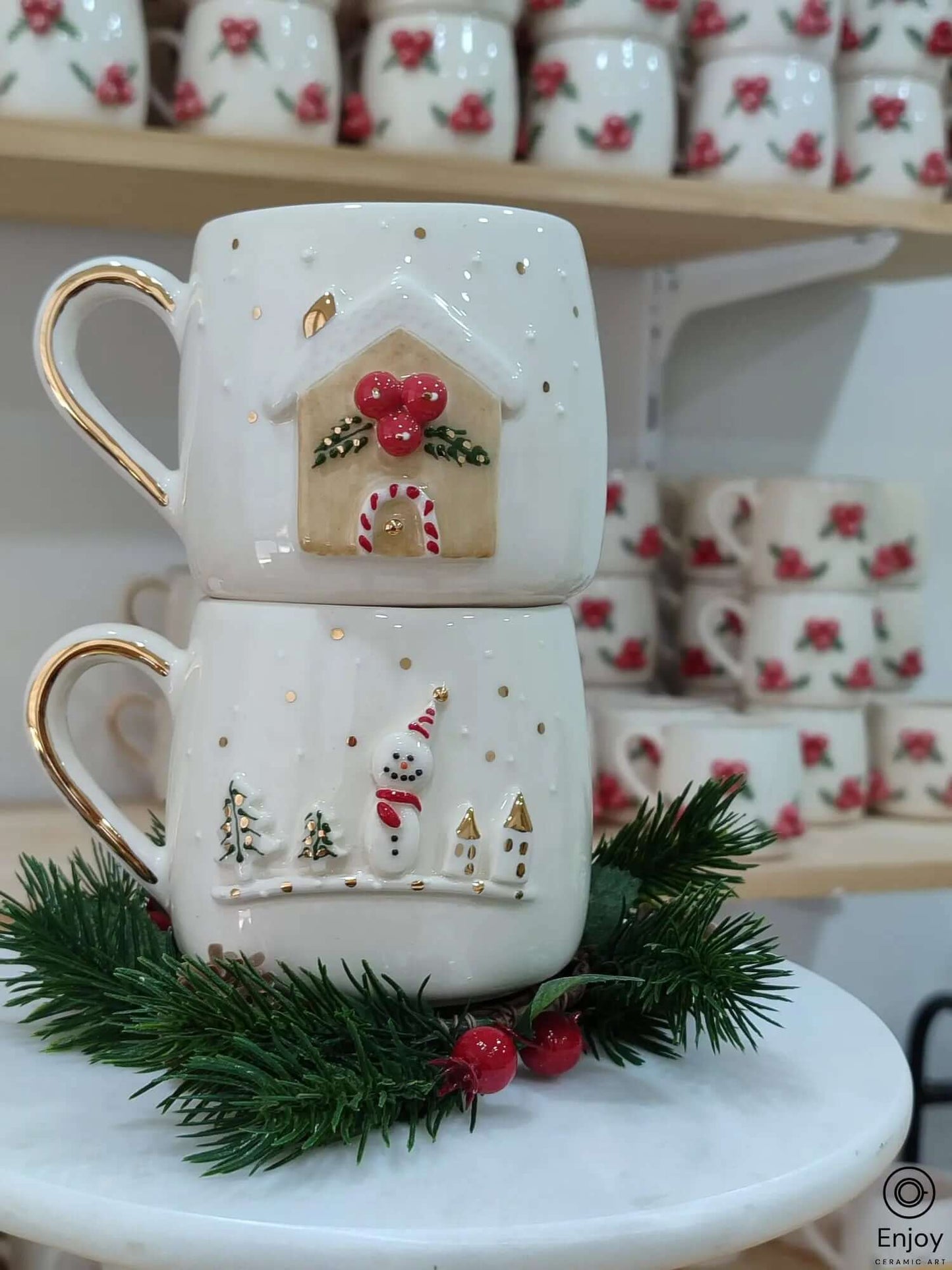 Handmade ceramic Christmas mug set featuring a 3D gingerbread house with festive details and a snowman in a winter scene, both with gold accents and handles.