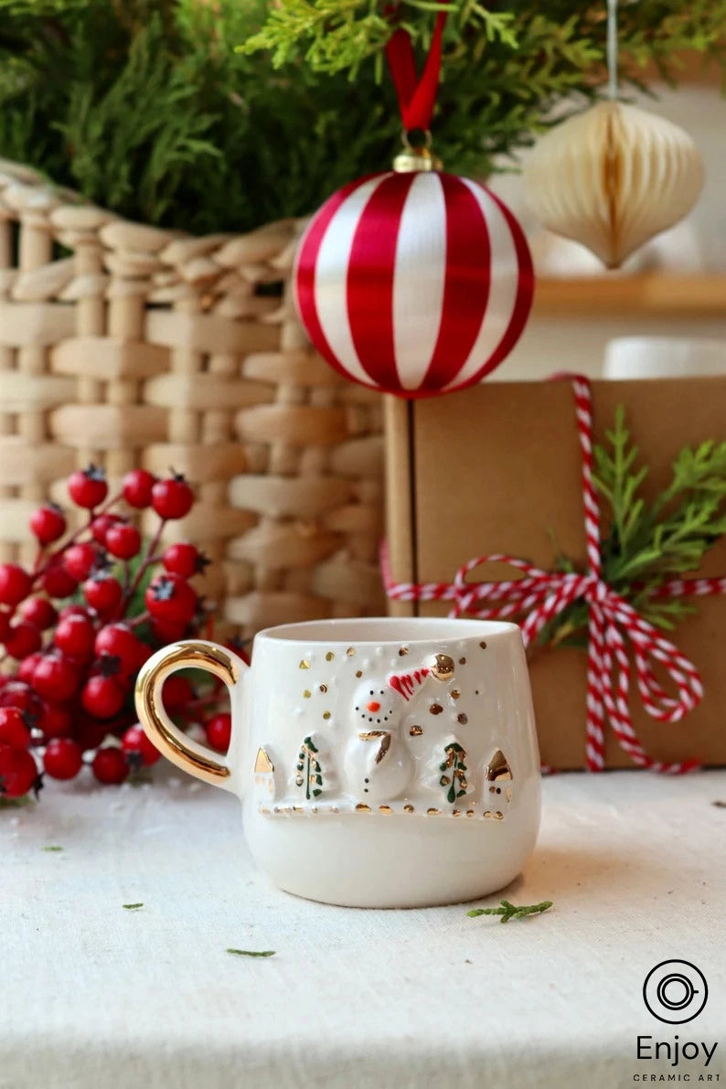 A charming espresso cup with a golden handle, featuring a raised snowman and tree motif, surrounded by festive holly berries and holiday decor.