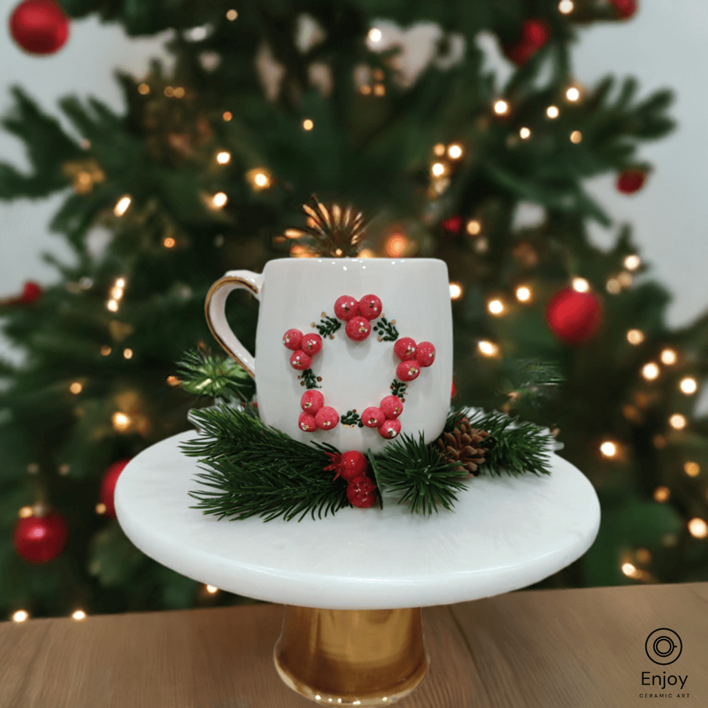 A white mug with a 3D red berry wreath on a golden stand, set against a lit Christmas tree