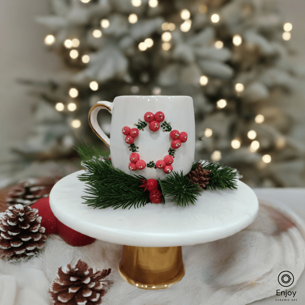 A chic white mug adorned with a festive 3D red berry wreath design, resting on a golden pedestal surrounded by pine sprigs and pinecones, with a softly lit Christmas tree in the background.