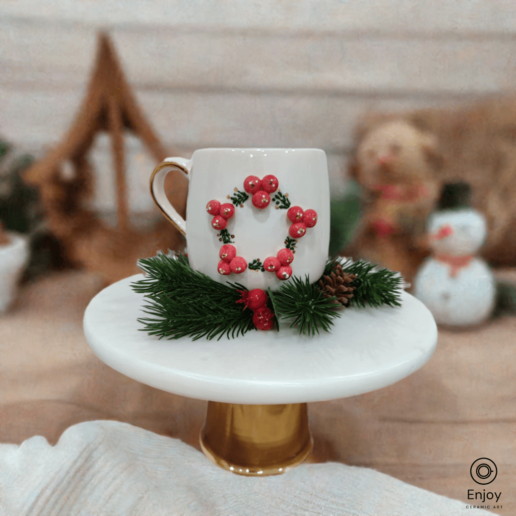 A white mug with a 3D red berry wreath sits on a golden stand, surrounded by festive decor