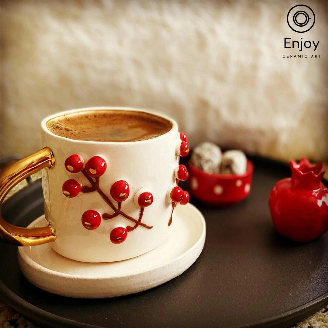 Rich espresso in a white ceramic cup with red winterberry design and gold handle, on a saucer placed on a dark tray, with a pomegranate-shaped container and truffles in the background.