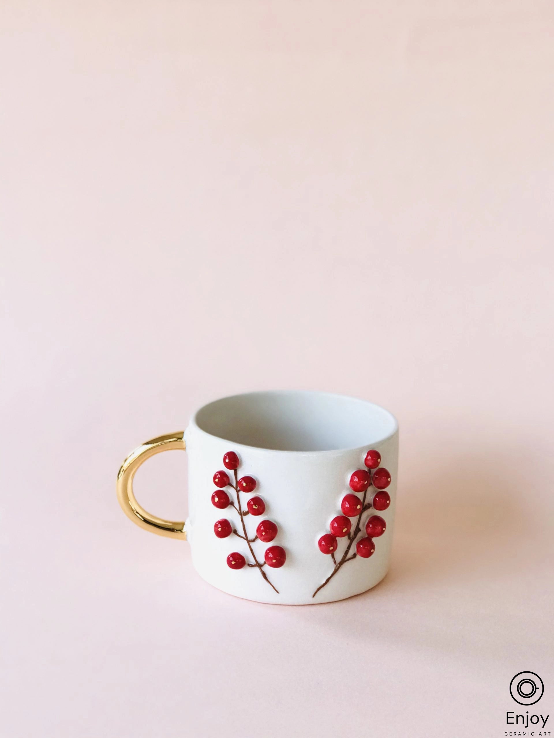 Elegant espresso cup with sculpted winterberry design and gold handle on a pink background, crafted by Enjoy Ceramic Art.