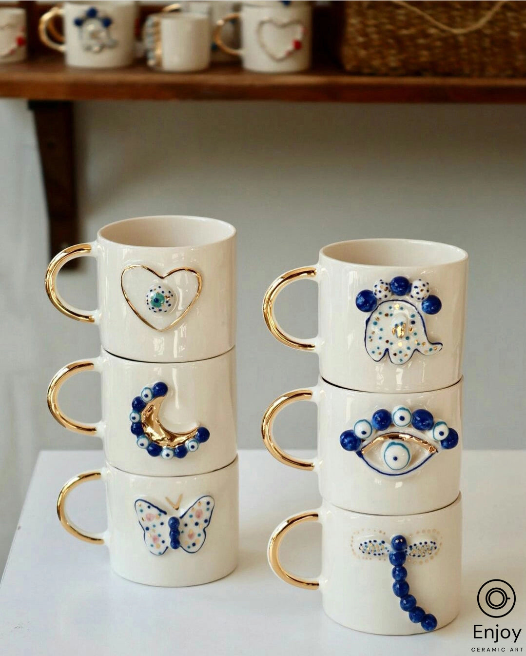 An elegant handmade ceramic espresso cup, featuring a blue crescent moon and evil eye motif, accented with gold on the handle, set against a white interior backdrop. The cup sits on a matching saucer, both with a glossy finish, showcasing artisanal craftsmanship