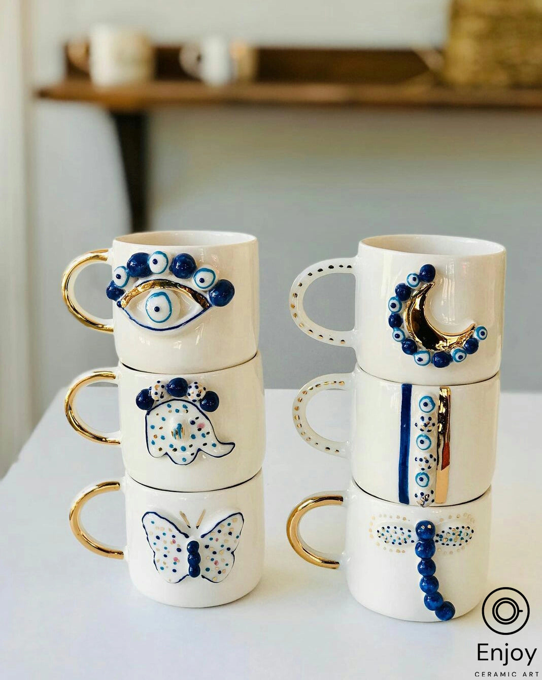 Coffee mugs with blue moon and evil eye design, gold handle, on saucer against a soft background, reflecting artisanal ceramic craft.