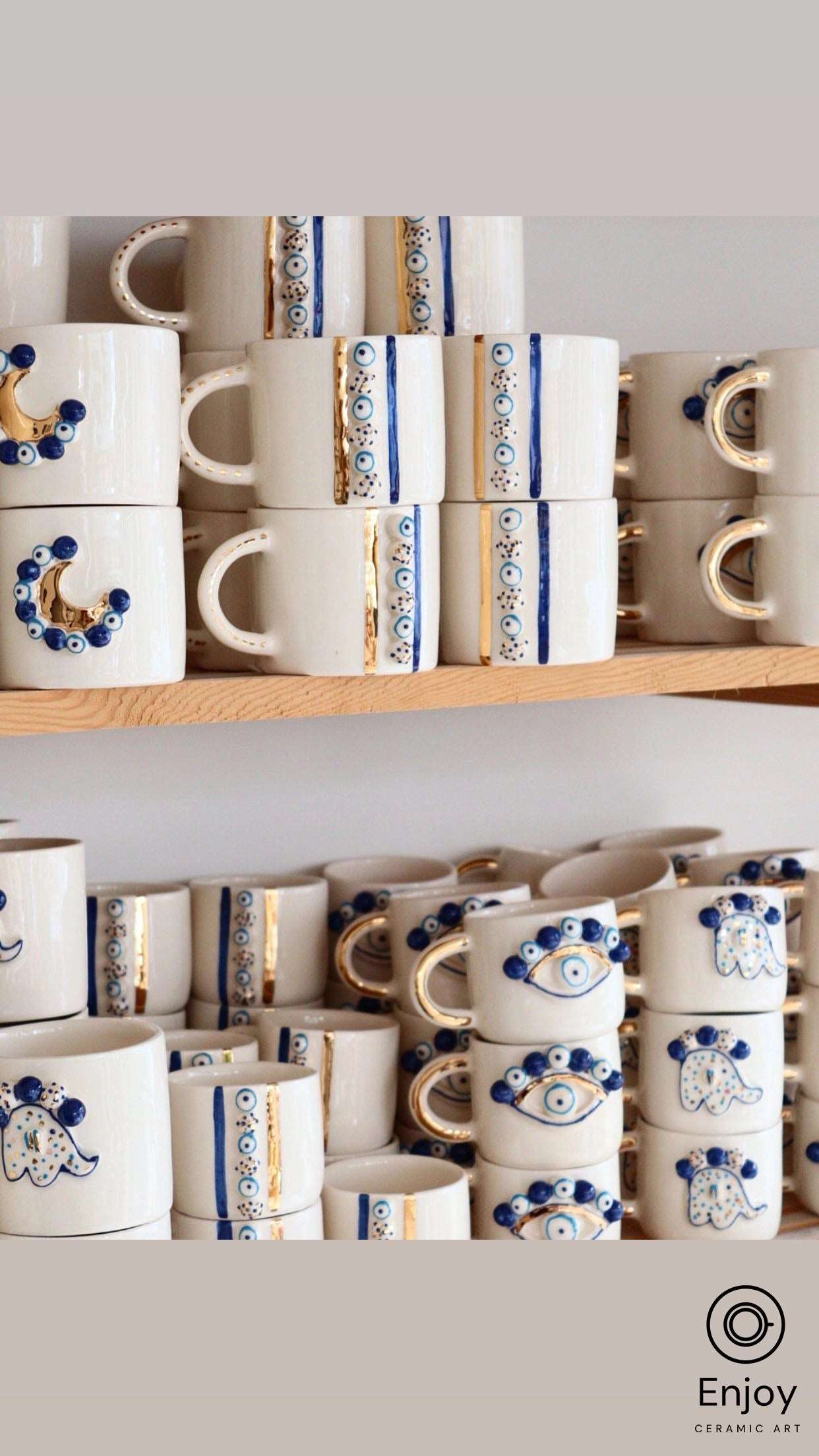 A collection of white ceramic mugs with golden accents and various blue evil eye designs neatly arranged on wooden shelves. The designs include crescent moons, hamsa hands, stripes of multiple evil eyes, and more, creating an aesthetically pleasing display with a cultural touch.