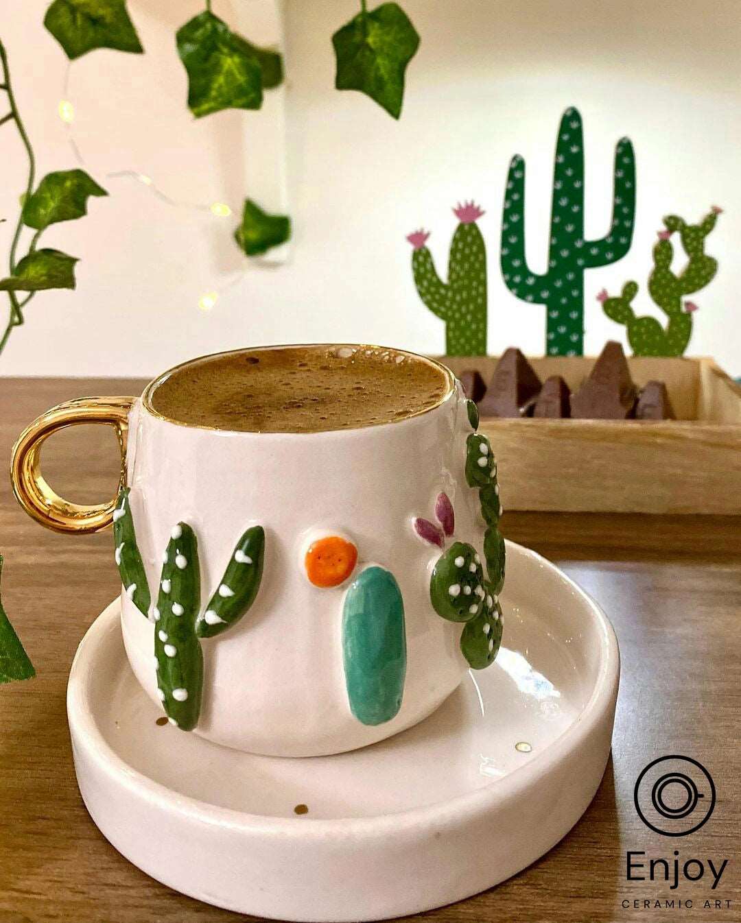 A mug with 3D cactus designs, a gold handle, and coffee, set against a backdrop of ivy and a cactus illustration.