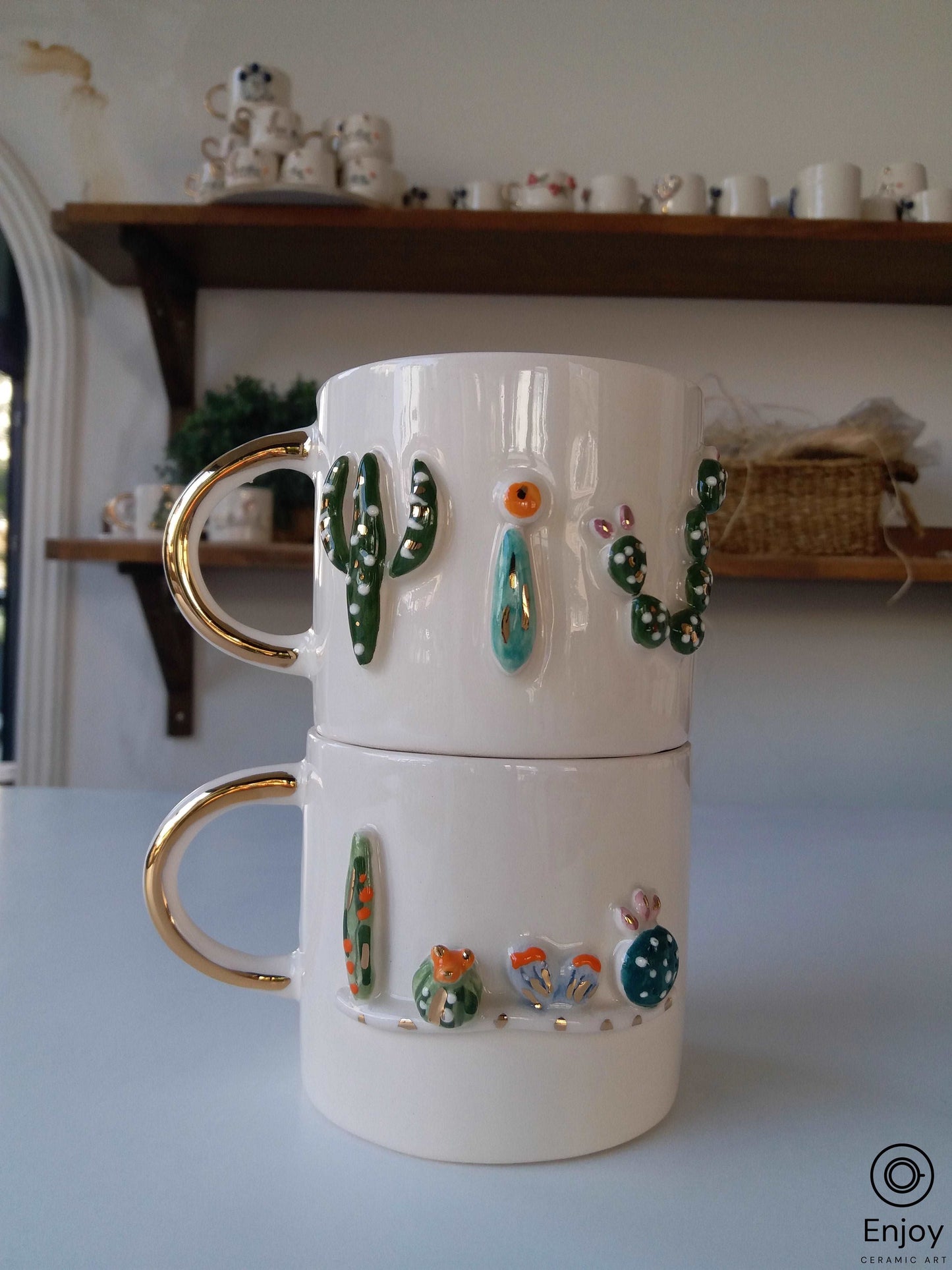 Stacked ceramic mugs with cactus designs and gold handles on a shelf.