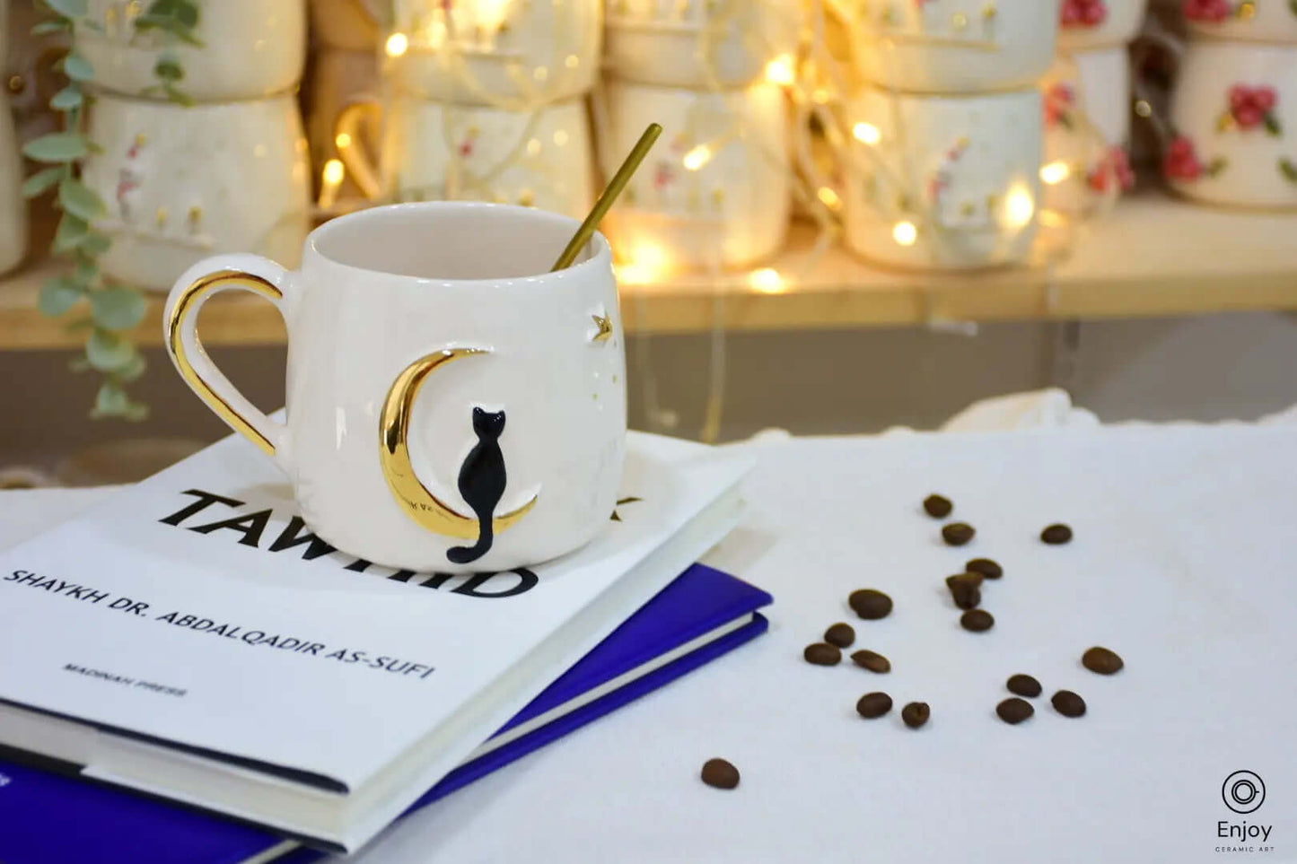 This celestial-themed mug, adorned with a black cat perched on a golden crescent moon, exudes a sense of mystery and charm. Perfect for those who enjoy a whimsical yet elegant touch to their coffee moments, it’s styled here with scattered coffee beans and a cozy stack of books, illuminated by warm fairy lights in the background. Ideal for quiet reflections or magical coffee breaks.