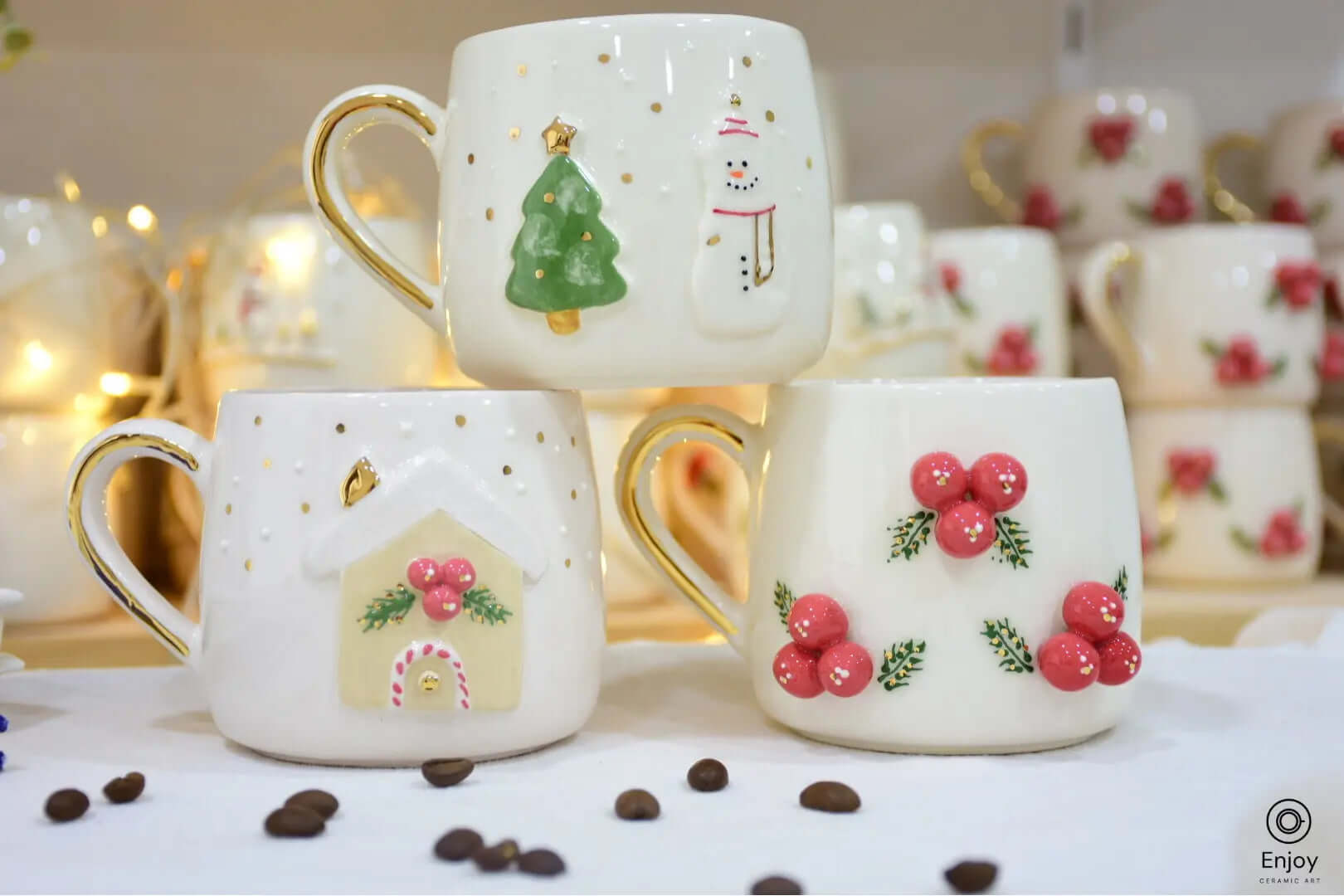 Set of three handmade Christmas-themed ceramic mugs featuring 3D designs: a snowman, a Christmas tree, and a gingerbread house with holly berries, each with a gold handle, displayed on a festive background with coffee beans and holiday decor.