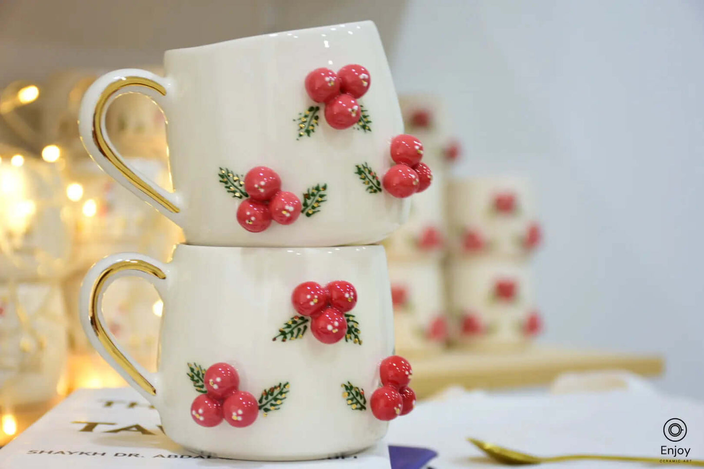 Stacked mugs adorned with vibrant red berries and green leaves, creating a festive, cozy vibe with warm fairy lights in the background.