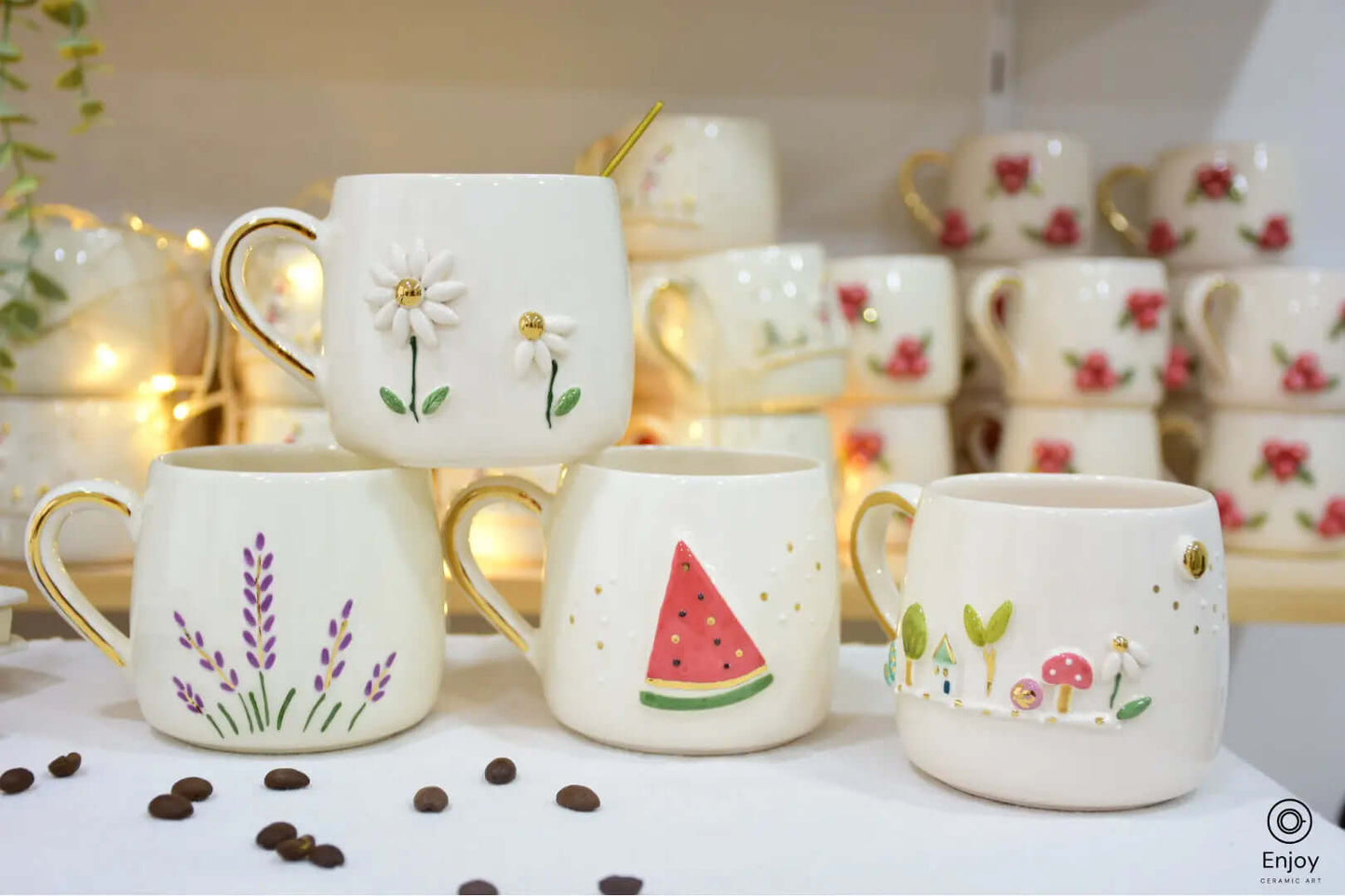 Set of four handmade ceramic mugs featuring daisy, lavender, watermelon, and garden designs, each with a gold handle, displayed against a cozy backdrop.