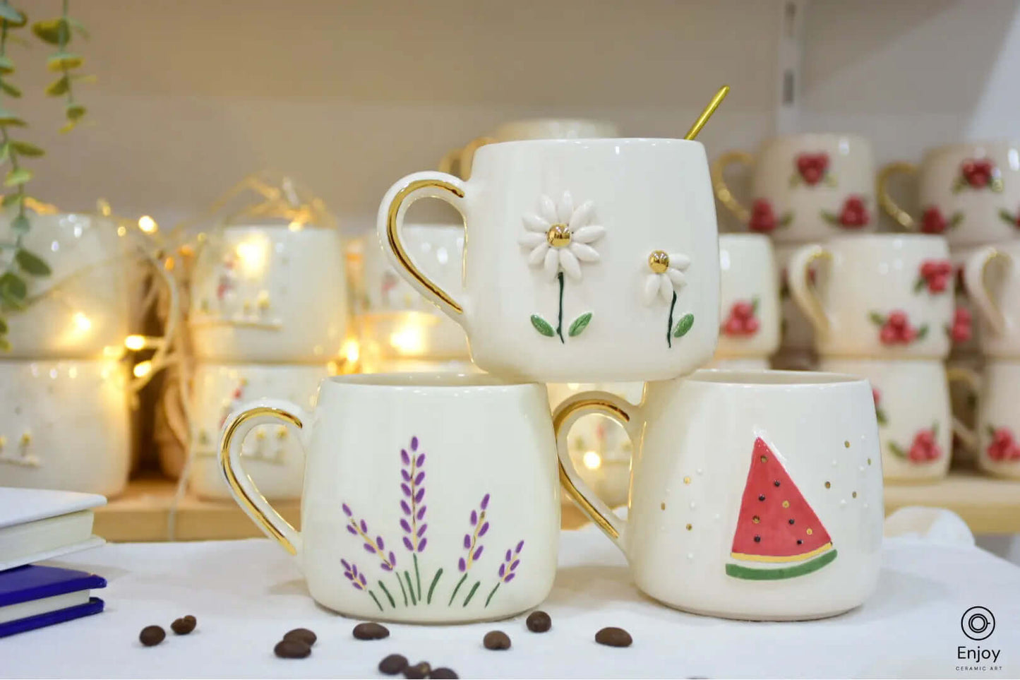 Handmade ceramic mug set featuring three 10 oz mugs with unique designs: a daisy with gold accents, lavender sprigs, and a watermelon slice, each with a gold handle.