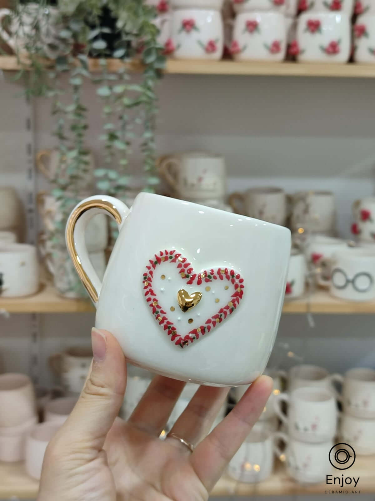 A handmade ceramic mug featuring a 3D heart design with a gold heart centerpiece, surrounded by a red floral frame, and a gold handle, perfect for gifts.