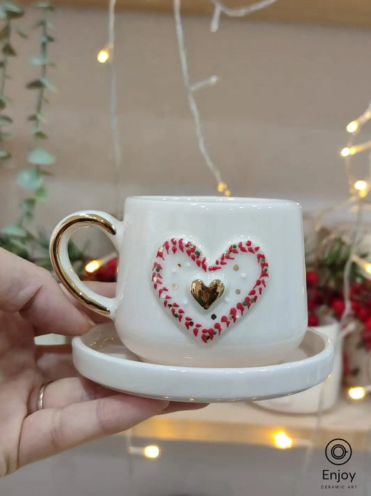 Hand holding a ceramic espresso cup with a 3D red and gold heart design, paired with a matching saucer, ideal for Valentine's Day or romantic occasions.