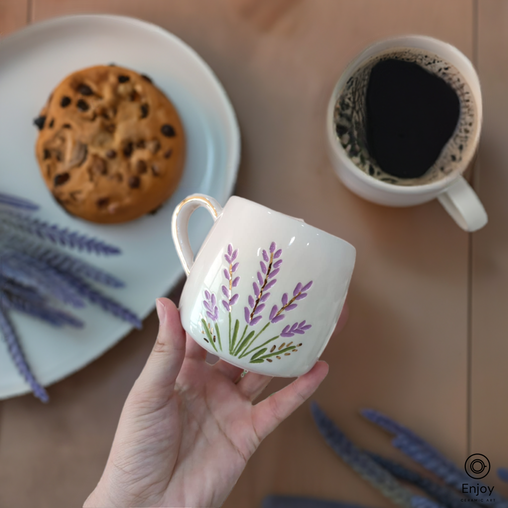 Handcrafted ceramic mug with a lavender design, gold handle, paired with a cookie and coffee setting.