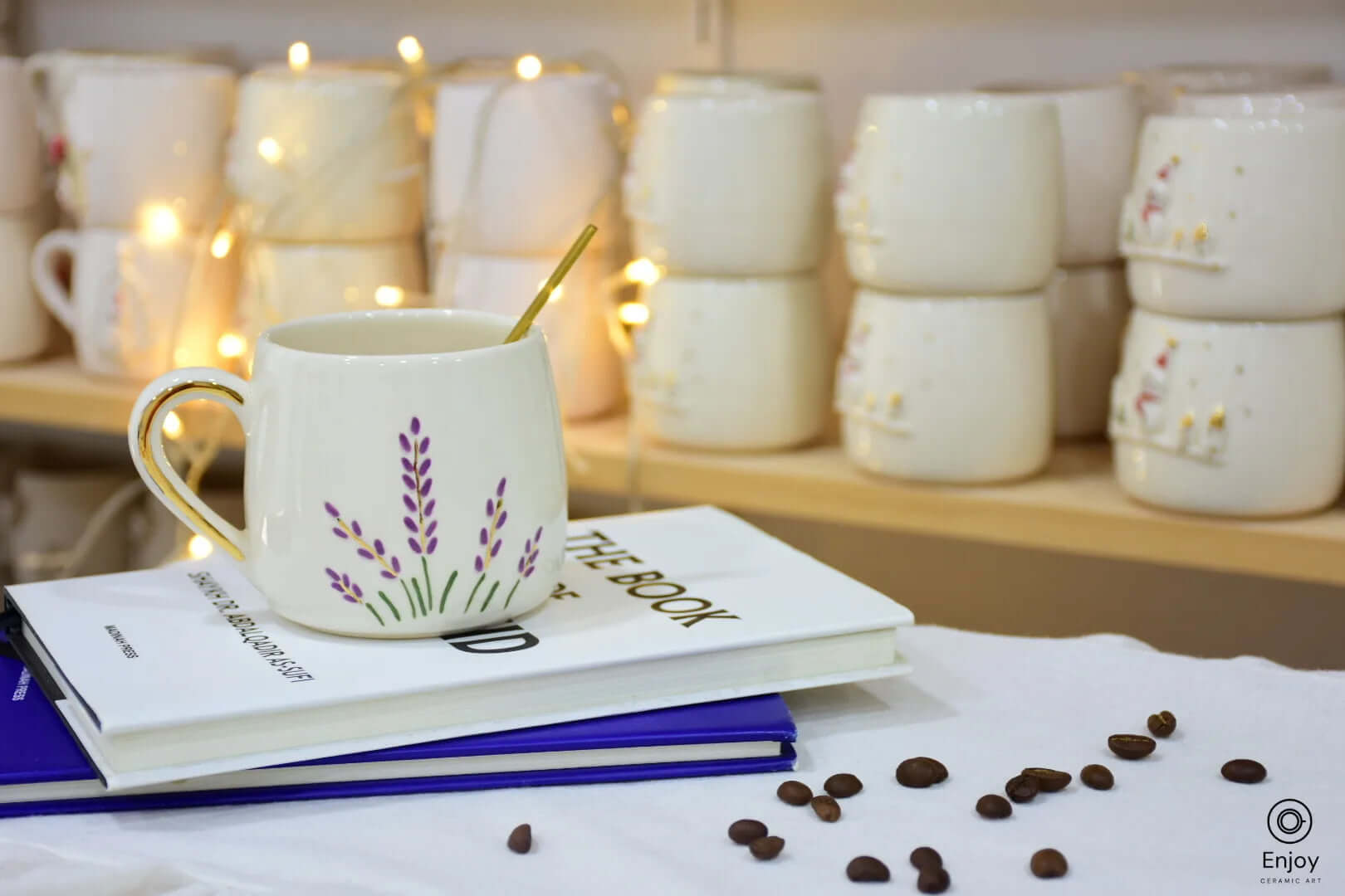 A ceramic mug adorned with lavender designs and a gold handle, resting on stacked books, surrounded by coffee beans and warm lights in the background.