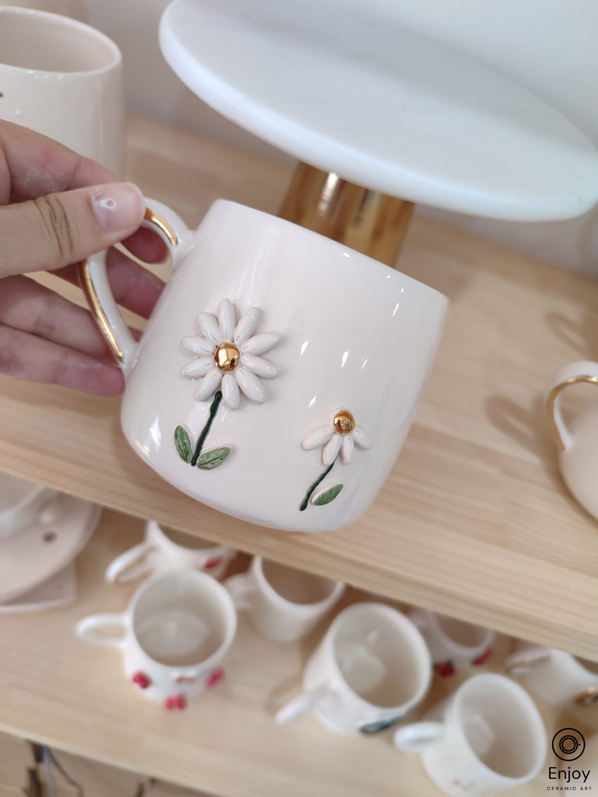 A close-up of a handmade daisy mug with two delicate flowers, gold accents, and a smooth ceramic finish.