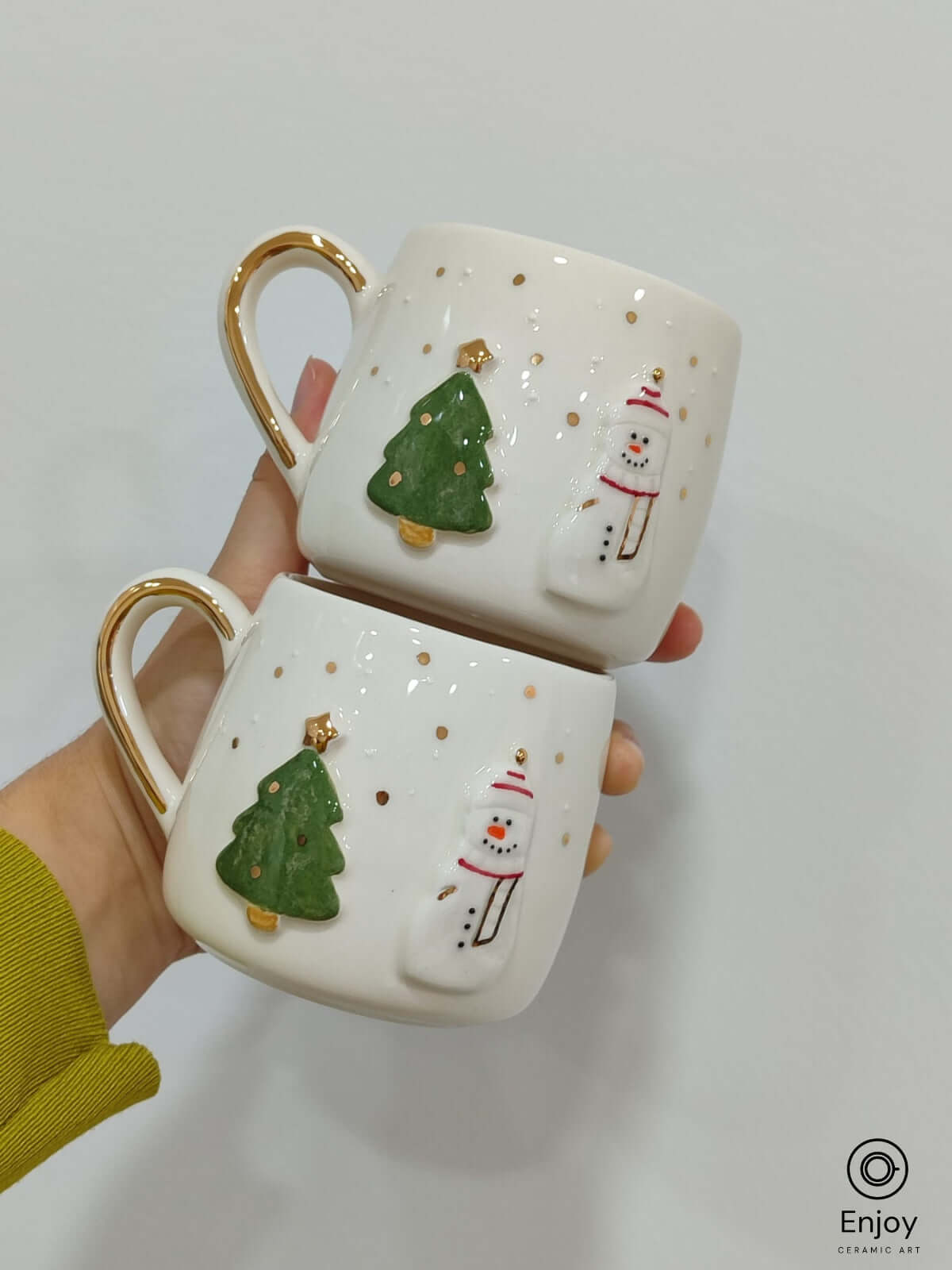 A festive pair of handmade ceramic mugs featuring a delightful snowman and Christmas tree design, with subtle golden accents for an added touch of elegance. Perfect for cozying up with a warm drink during the holiday season or sharing holiday cheer with loved ones.