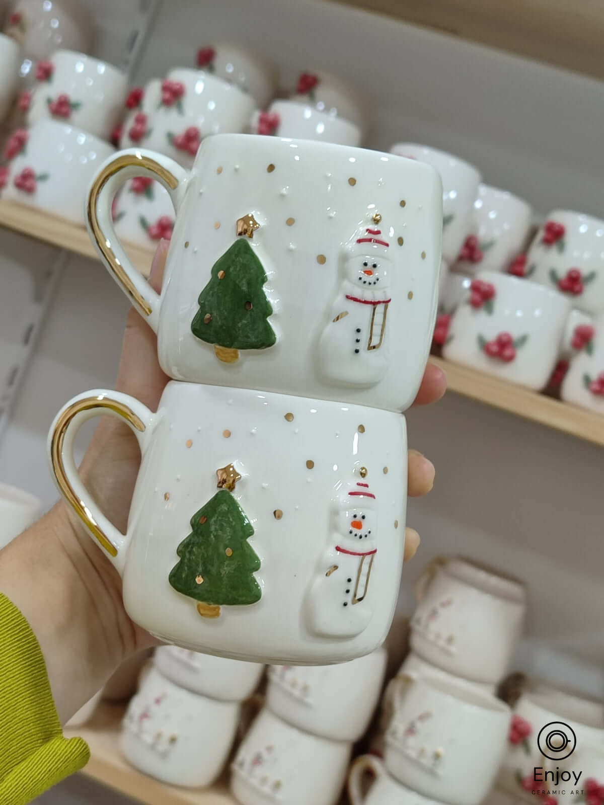 A pair of handmade ceramic mugs featuring a festive holiday design with a snowman and a Christmas tree, adorned with golden accents on the handles. Perfect for bringing a touch of warmth and cheer to your holiday gatherings or gifting to loved ones during the season.