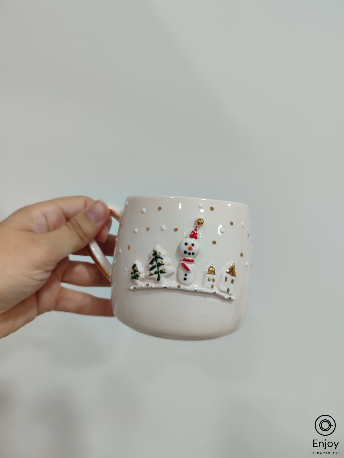 A chic white mug adorned with a 3D snowman, little houses, trees  with gold details on a white background