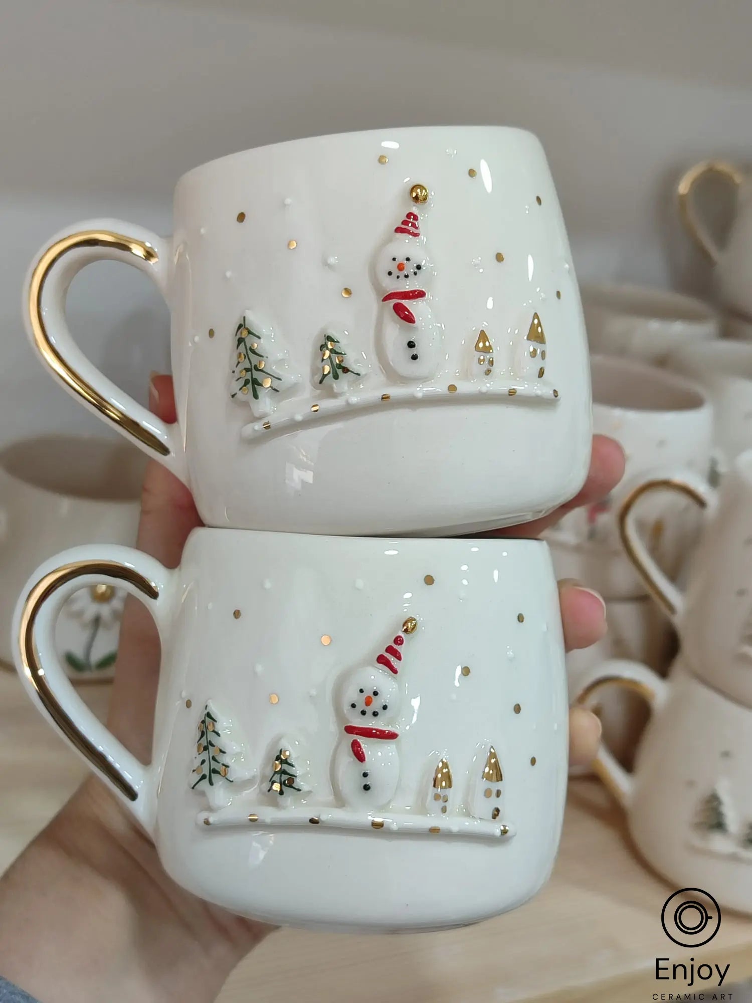 Handmade ceramic mugs showcasing a delightful snowman in a cozy winter village scene, surrounded by snowy trees and golden-roofed houses. The gold-accented handle adds a touch of elegance, perfect for enjoying warm drinks during the festive season.