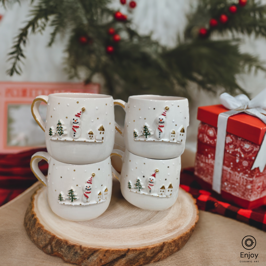 A set of four festive ceramic mugs featuring a charming snowman and winter village design, stacked on a rustic wooden slab, with Christmas décor and gift boxes in the background.