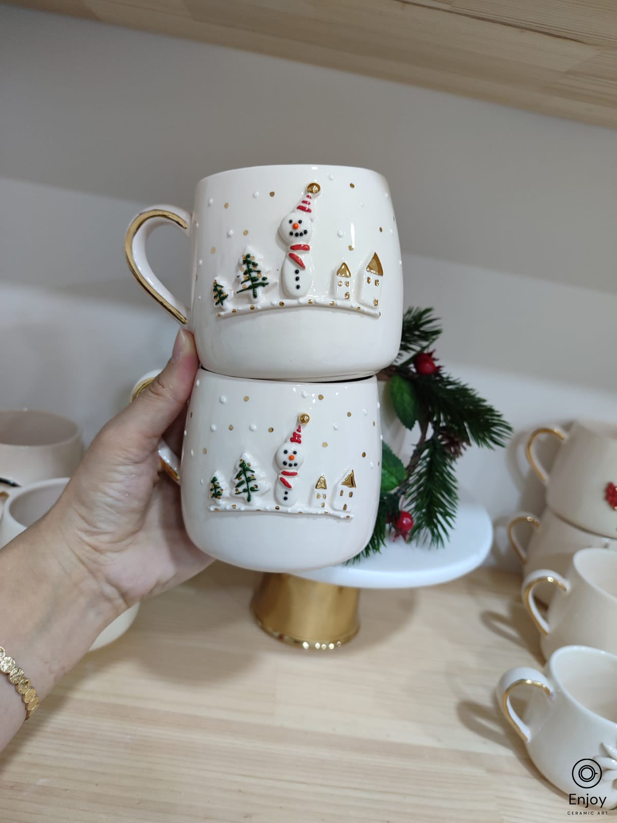 A chic white mugs adorned with a 3D snowman, little houses, trees with gold details on a shelve