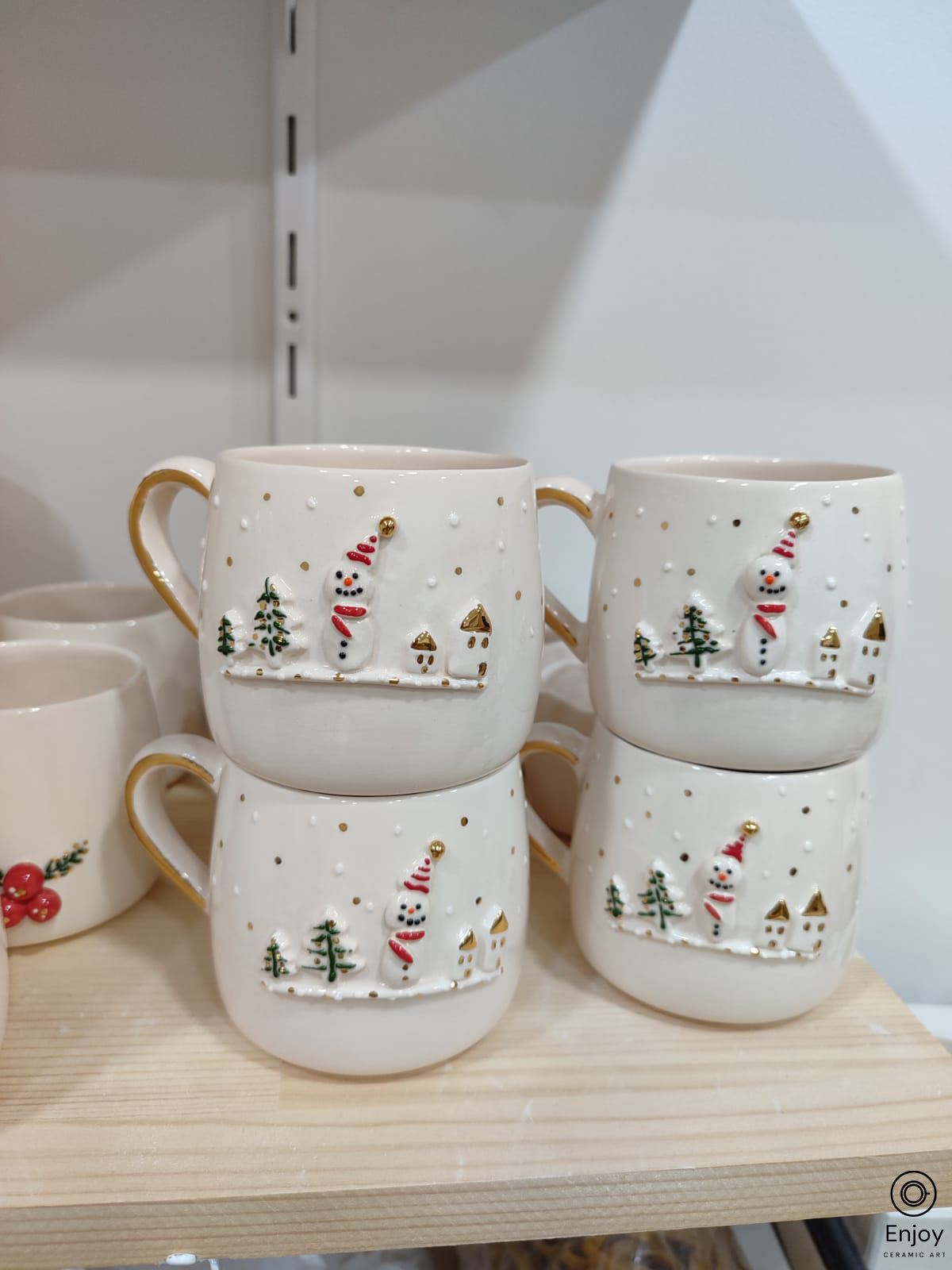 A chic white mugs adorned with a 3D snowman, little houses, trees with gold details on a shelve