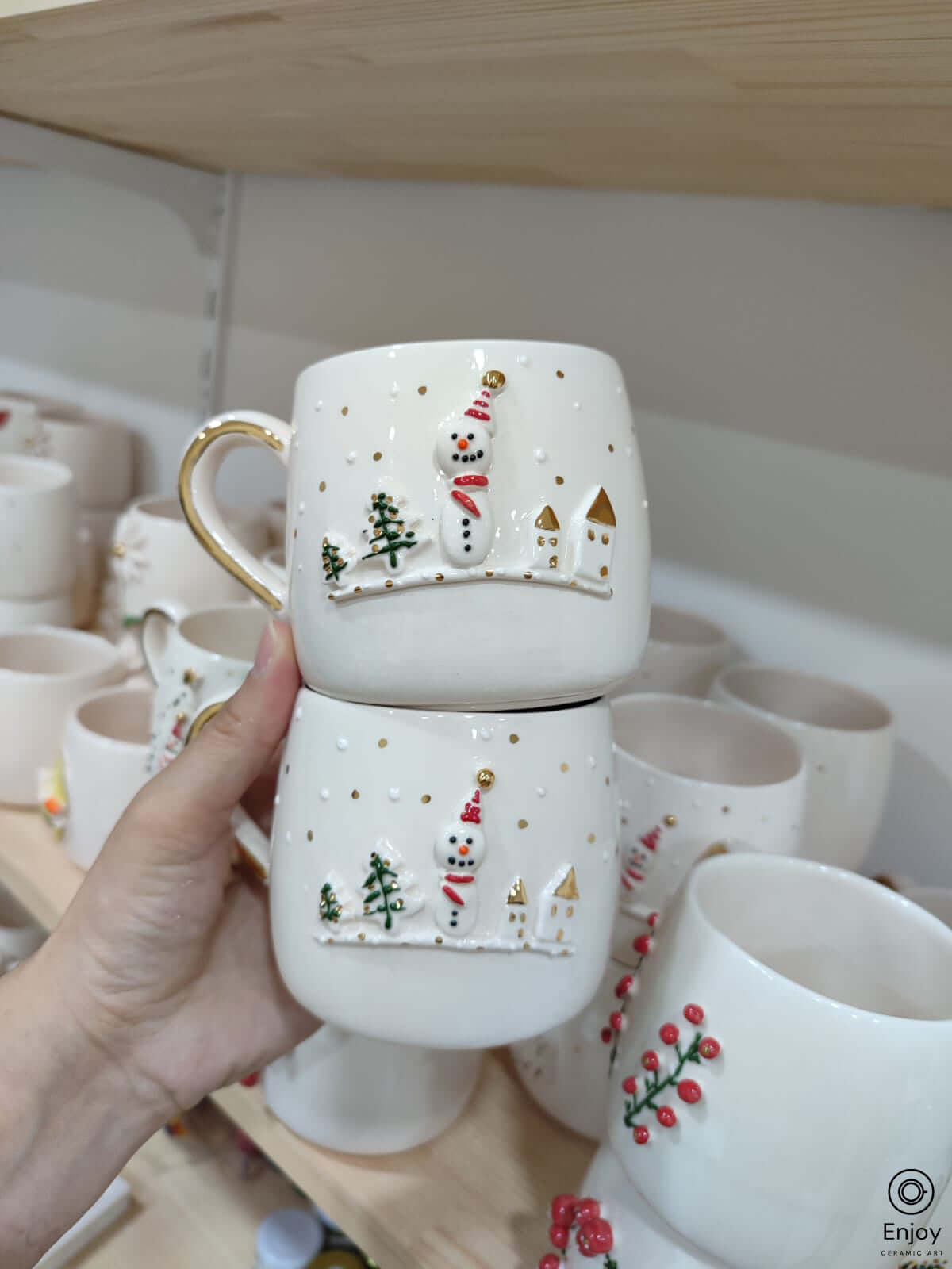 A chic white mugs adorned with a 3D snowman, little houses, trees with gold details on a shelve