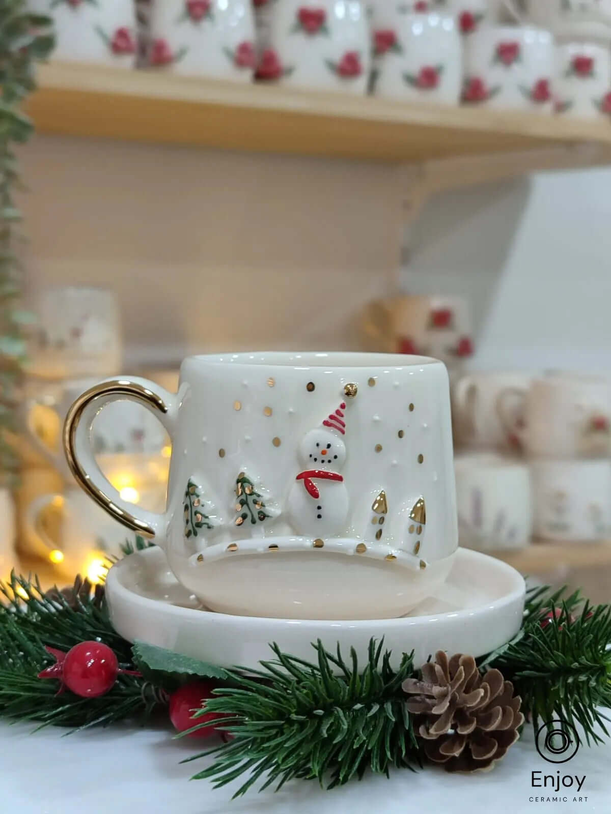 Festive snowman-themed espresso cup with gold accents, paired with a saucer, nestled in holiday greenery for a cozy Christmas vibe.