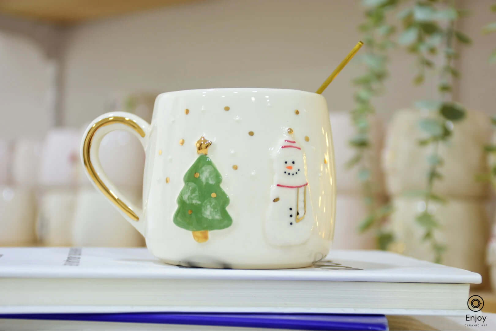 A festive ceramic mug featuring a snowman and Christmas tree design, accented with gold dots and a golden handle, perfect for holiday cheer.