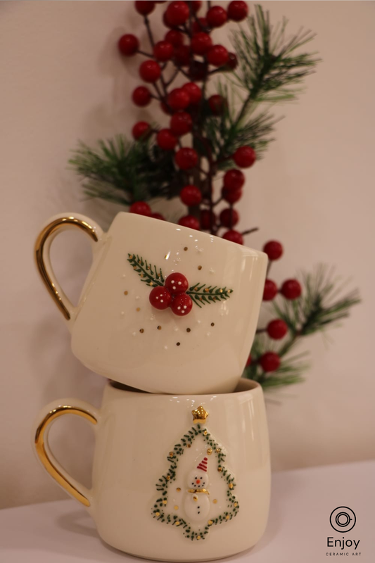 Two stacked mugs with Christmas designs against a blurred background of red berries and greenery.