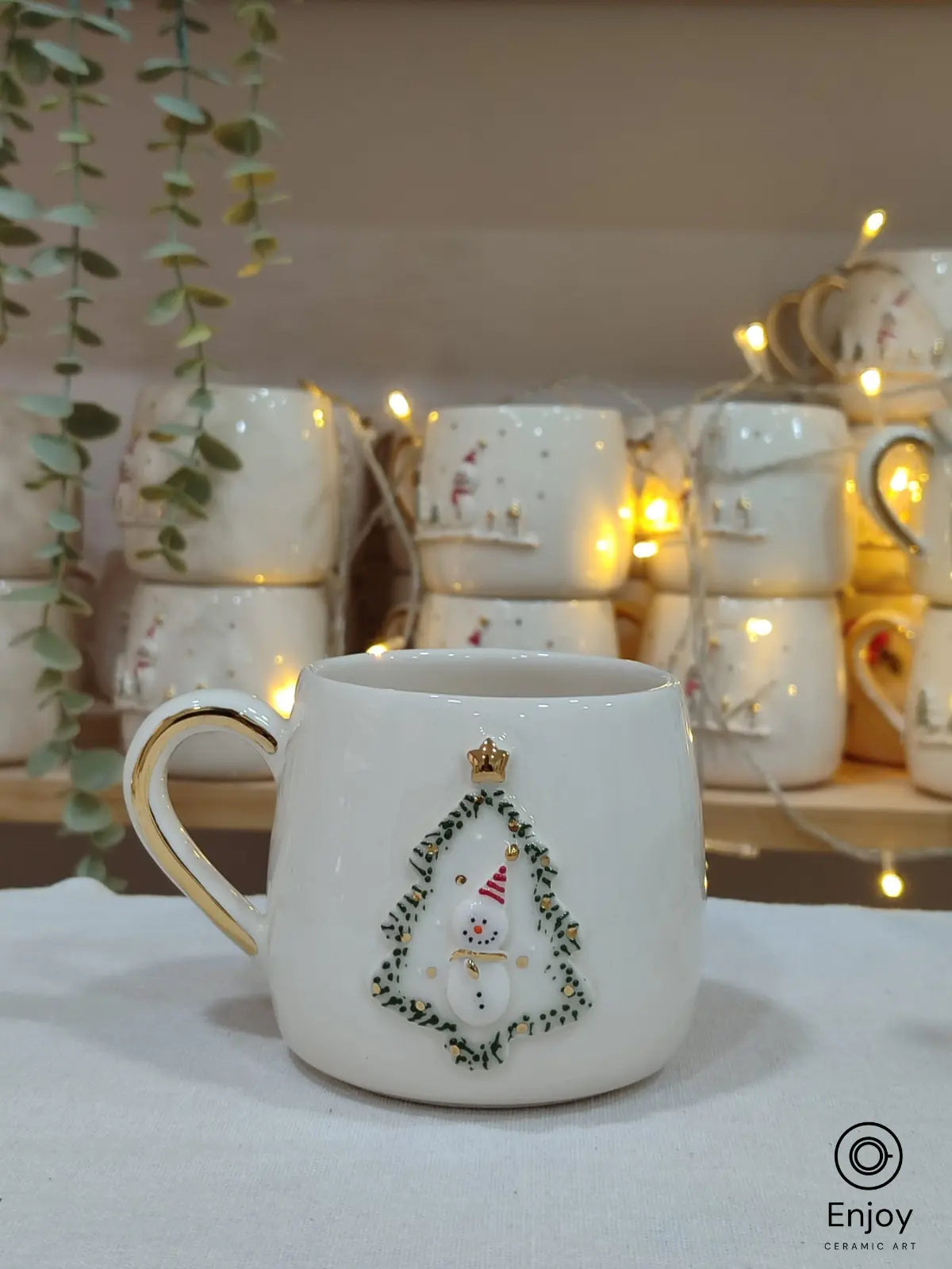 This festive mug features a snowman in a Christmas tree frame with gold accents, perfect for adding holiday cheer or gifting loved ones!