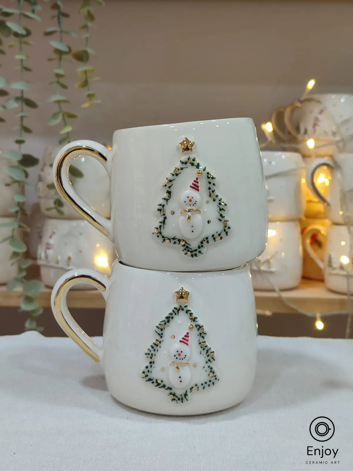 Two handcrafted ceramic mugs with a festive snowman framed in a Christmas tree design, adorned with gold accents, perfect for holiday gifting!