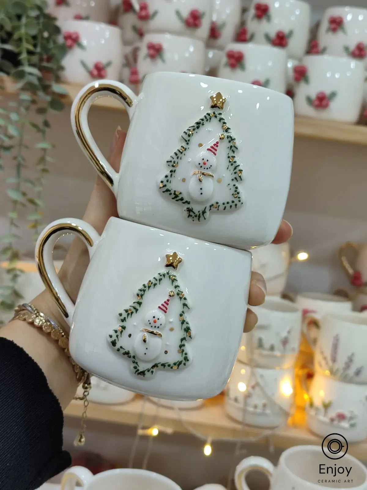 Two elegant handmade ceramic mugs featuring a snowman in a Christmas tree frame. A perfect festive gift adorned with gold accents!