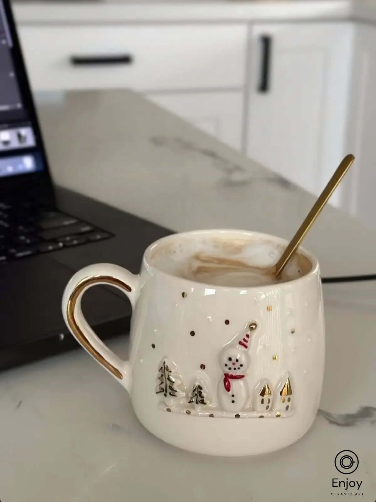 A cozy moment captured with a handmade ceramic mug featuring an adorable snowman design and golden accents, perfect for enjoying a warm latte. The delicate snowman details bring a festive touch, making it an ideal companion for holiday mornings or a charming addition to your winter workspace.