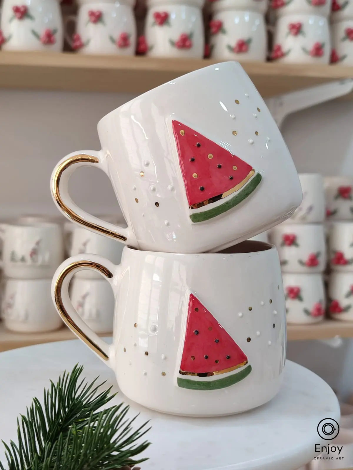 Handmade ceramic mugs featuring a vibrant watermelon slice design, displayed on a marble stand with festive decor.