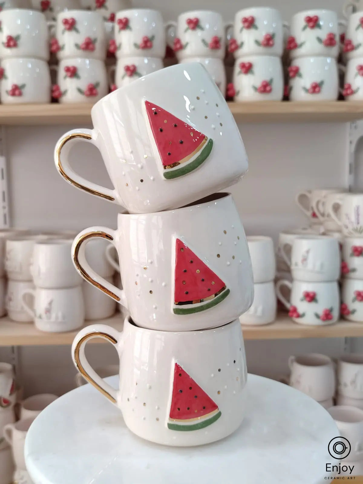 Handmade ceramic mugs featuring a vibrant watermelon slice design, displayed on a marble stand.