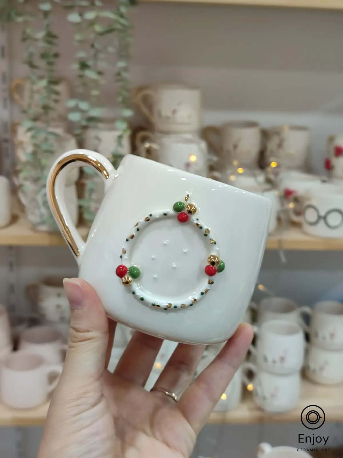 A handmade ceramic mug featuring a 3D Christmas wreath design with red, green, and gold accents, paired with a gold handle, perfect for holiday celebrations.